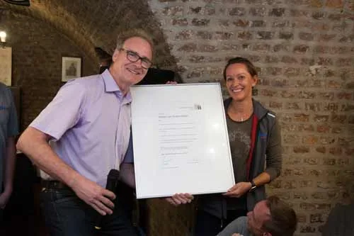 Ein Mann und eine Frau halten eine weiße Tafel vor einer Backsteinwand.