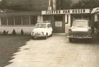 Ein Schwarzweißfoto von zwei vor einem Gebäude geparkten Autos.